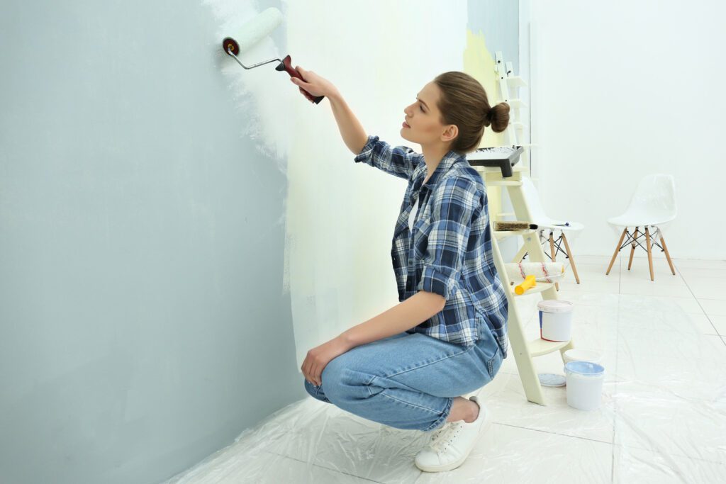 Young woman painting wall in room