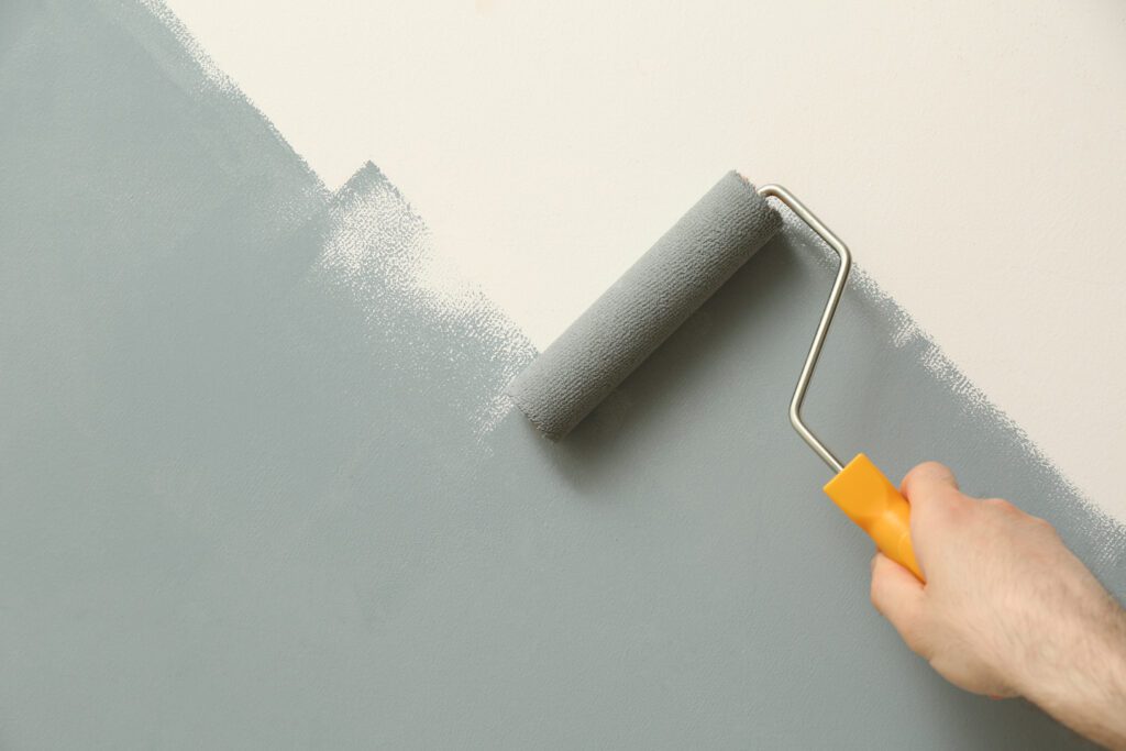 Applying grey paint with roller brush on white wall